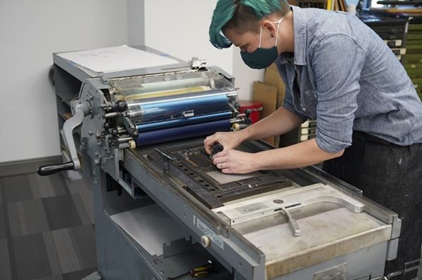 person with teal hair working on a Vandercook SP-15 printing press