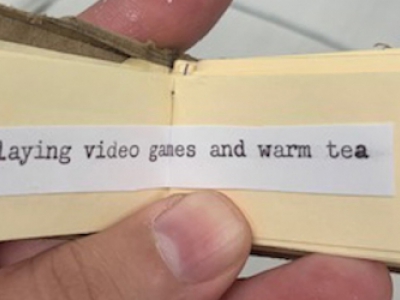 tiny book open to page reading "playing video games and warm tea"